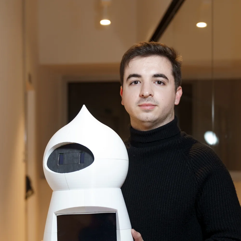 Adrián González, fundador de Lopako, junto al primer prototipo: un robot blanco en forma de gota con pantalla.